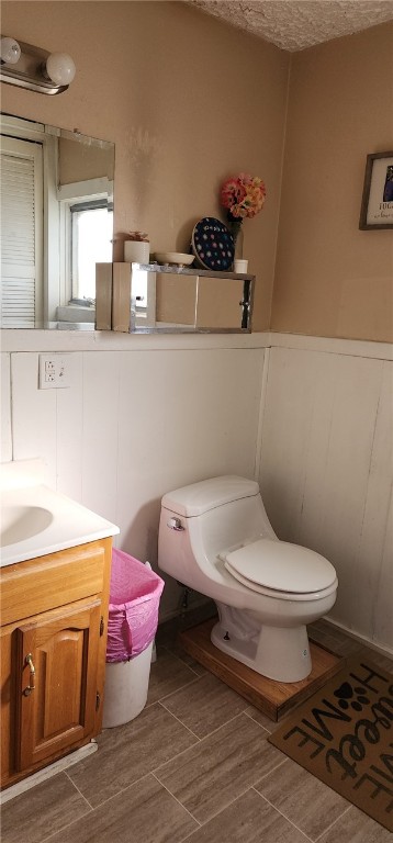 half bath with a textured ceiling, toilet, vanity, and wood tiled floor