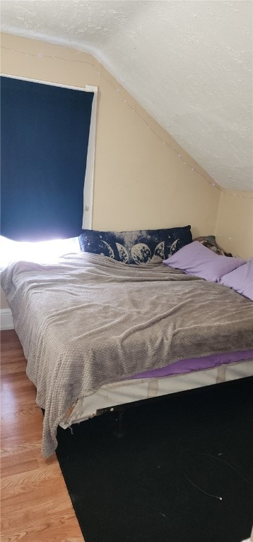 bedroom with light wood finished floors, a textured ceiling, and lofted ceiling