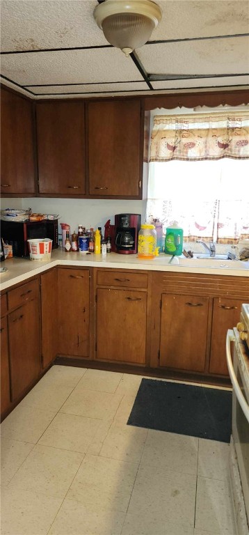 kitchen featuring light countertops, range, brown cabinets, and a sink