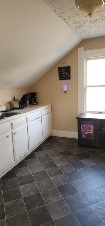 kitchen with white cabinetry, lofted ceiling, baseboards, and a sink