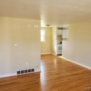 unfurnished room featuring wood finished floors, visible vents, and baseboards