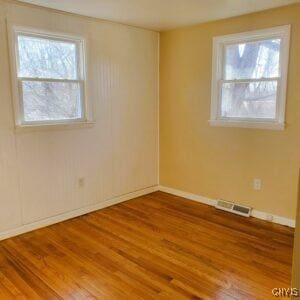 empty room with visible vents, a healthy amount of sunlight, baseboards, and wood finished floors