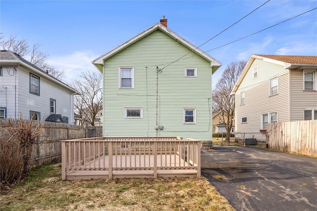 back of house featuring a wooden deck, a chimney, driveway, and fence