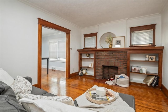 living room featuring a brick fireplace, crown molding, baseboards, and wood finished floors