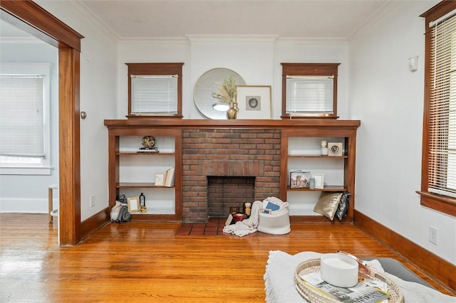 living area featuring a fireplace, crown molding, baseboards, and wood finished floors