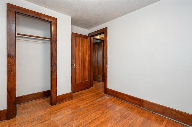 unfurnished bedroom featuring a closet, a textured ceiling, baseboards, and wood finished floors