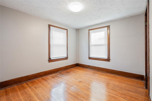 empty room featuring a textured ceiling, baseboards, and light wood-style floors