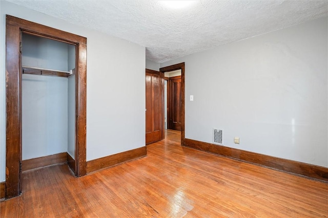 unfurnished bedroom with visible vents, baseboards, light wood-type flooring, a closet, and a textured ceiling