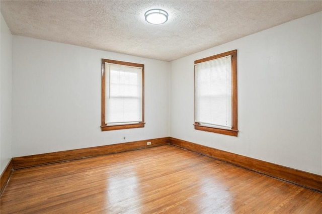 empty room with a textured ceiling, light wood-type flooring, and baseboards