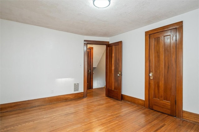 unfurnished bedroom featuring light wood-type flooring, visible vents, a textured ceiling, a closet, and baseboards