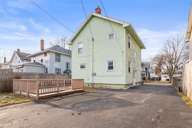 rear view of property featuring a residential view, a chimney, a deck, and fence