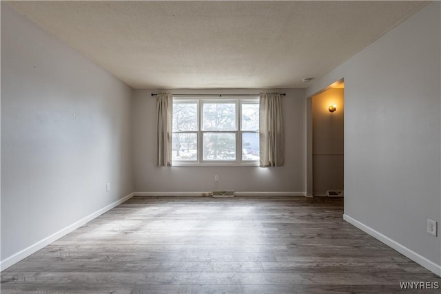 spare room with visible vents, a textured ceiling, baseboards, and wood finished floors