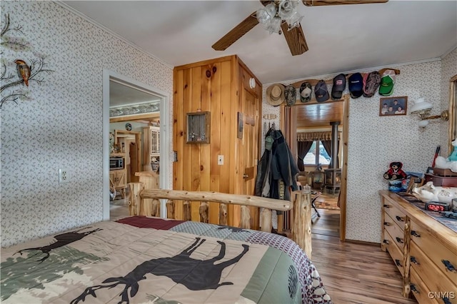 bedroom with ceiling fan, wood finished floors, crown molding, and wallpapered walls