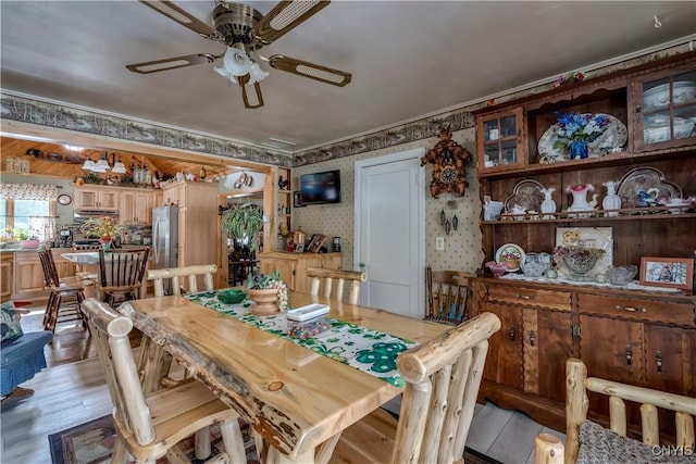 dining space featuring wood finished floors, ceiling fan, ornamental molding, and wallpapered walls