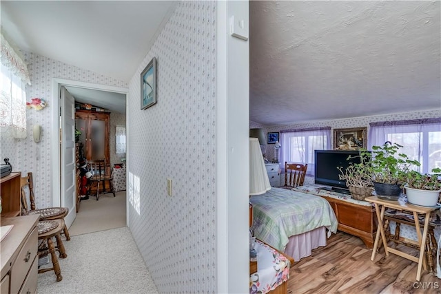 corridor featuring wallpapered walls, lofted ceiling, wood finished floors, and a textured ceiling