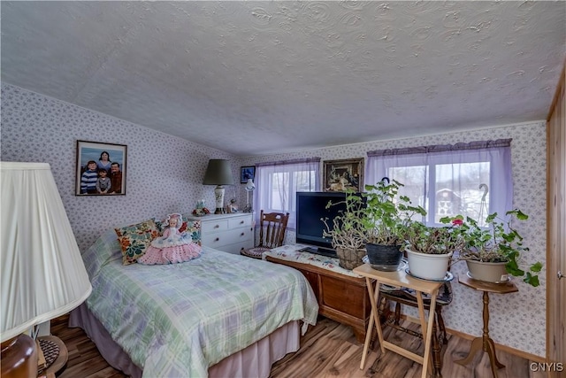 bedroom with wallpapered walls, vaulted ceiling, wood finished floors, and a textured ceiling