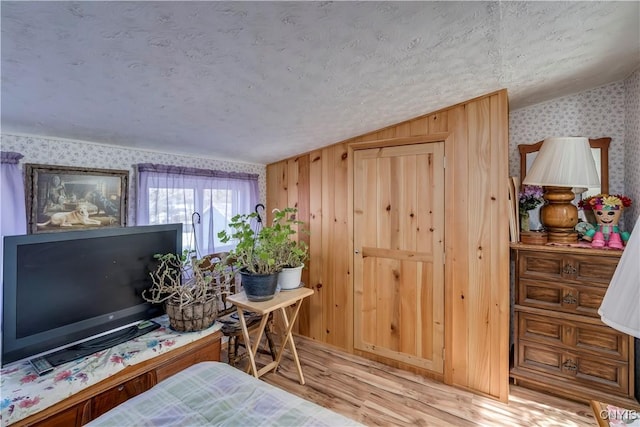 bedroom with a textured ceiling, wood finished floors, vaulted ceiling, and wallpapered walls