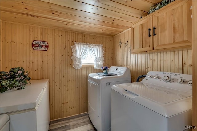 clothes washing area featuring cabinet space, light wood-style floors, wood ceiling, and washing machine and dryer