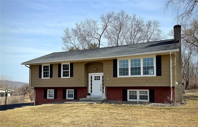 bi-level home with brick siding, a chimney, a front lawn, and fence