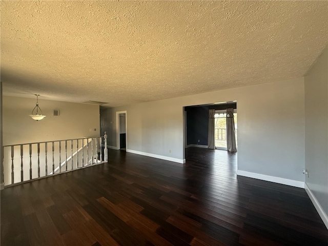 spare room featuring visible vents, a textured ceiling, baseboards, and dark wood-style flooring