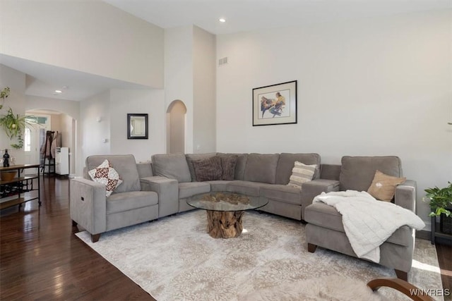 living room featuring arched walkways, visible vents, a towering ceiling, and wood finished floors