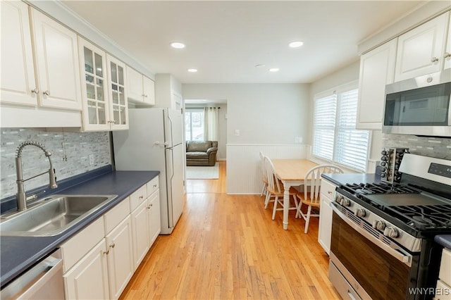 kitchen featuring a sink, dark countertops, appliances with stainless steel finishes, wainscoting, and light wood finished floors