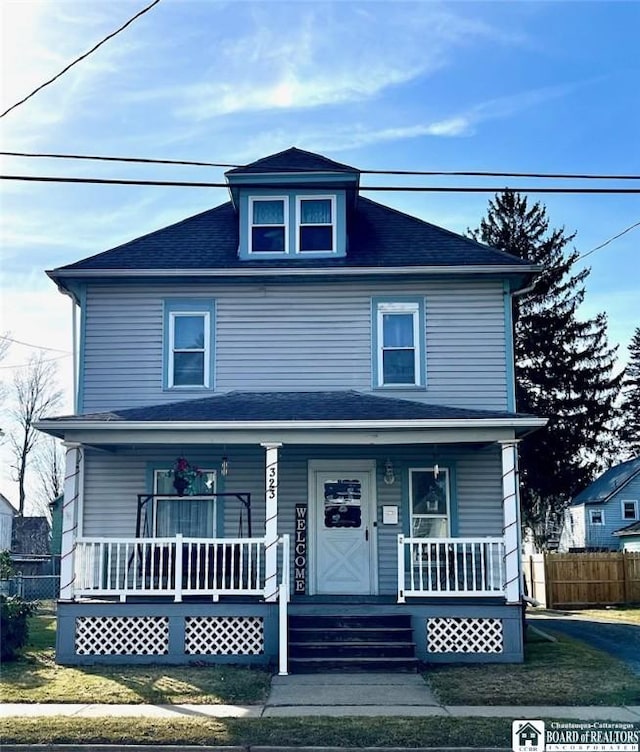 american foursquare style home with covered porch, roof with shingles, and fence