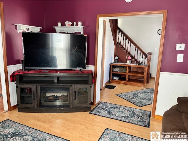 living area with stairs, wood finished floors, and wainscoting