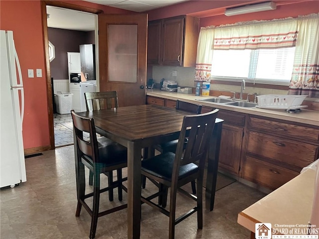 kitchen featuring washer / dryer, light countertops, freestanding refrigerator, and a sink