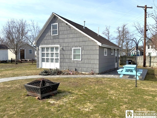 view of property exterior featuring a lawn, fence, and an outdoor fire pit