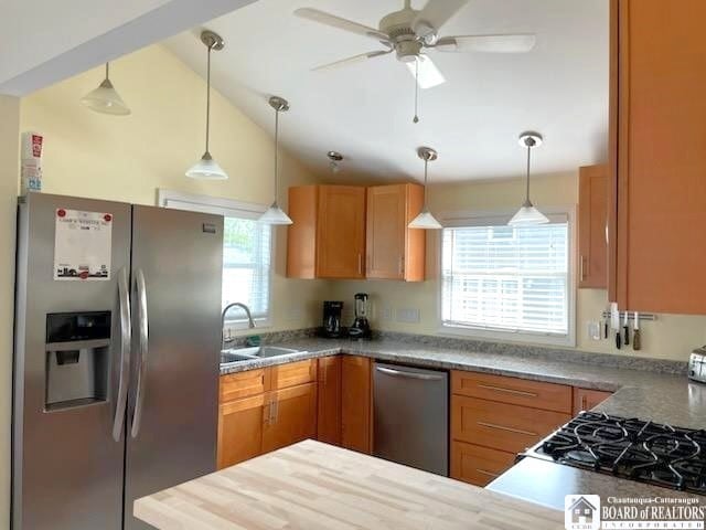 kitchen featuring lofted ceiling, ceiling fan, a sink, appliances with stainless steel finishes, and pendant lighting