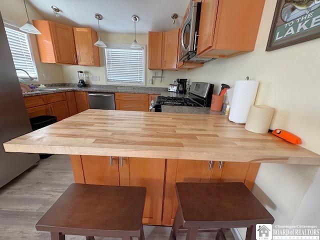 kitchen with a kitchen bar, a sink, wood counters, appliances with stainless steel finishes, and a peninsula