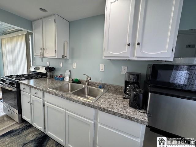 kitchen with dark wood-type flooring, black microwave, stainless steel range with gas stovetop, white cabinets, and a sink