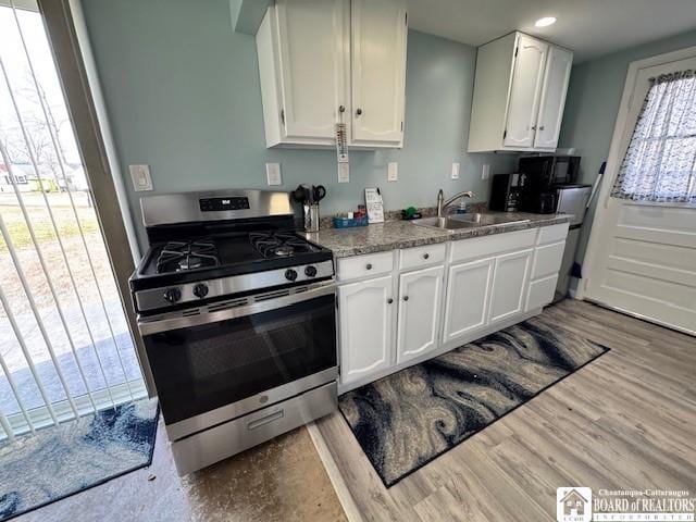 kitchen featuring stainless steel range with gas stovetop, white cabinets, wood finished floors, and a sink