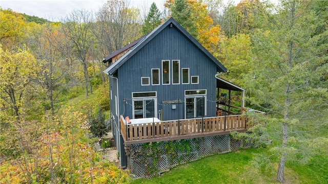 rear view of house with a deck, a view of trees, and a lawn