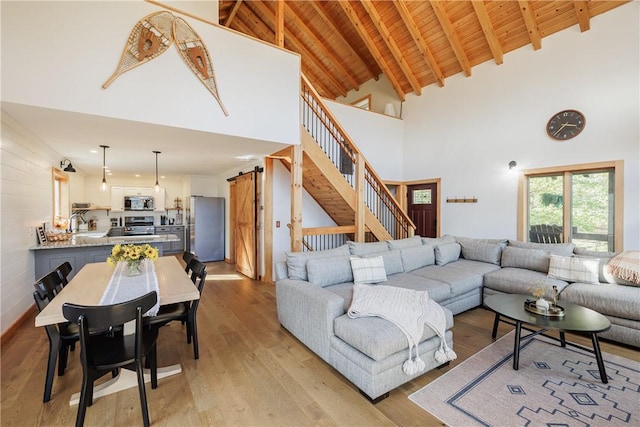 living area featuring stairs, a barn door, beam ceiling, light wood-style flooring, and wooden ceiling