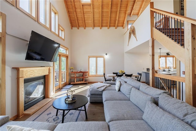 living room featuring stairway, beam ceiling, wooden ceiling, wood finished floors, and a glass covered fireplace