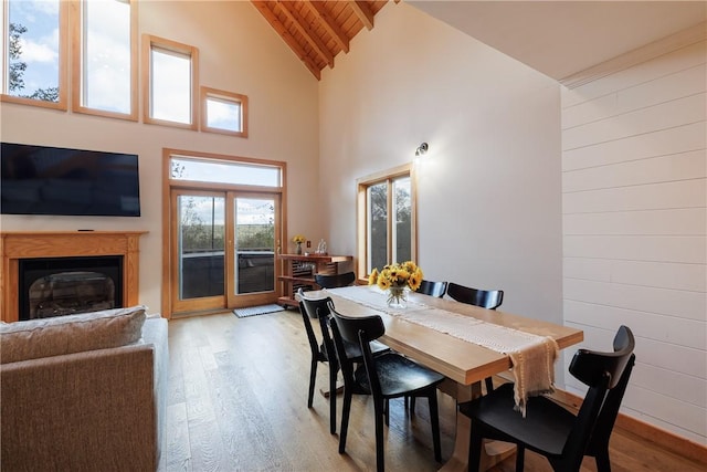 dining room featuring light wood-type flooring, wooden walls, wood ceiling, and a glass covered fireplace