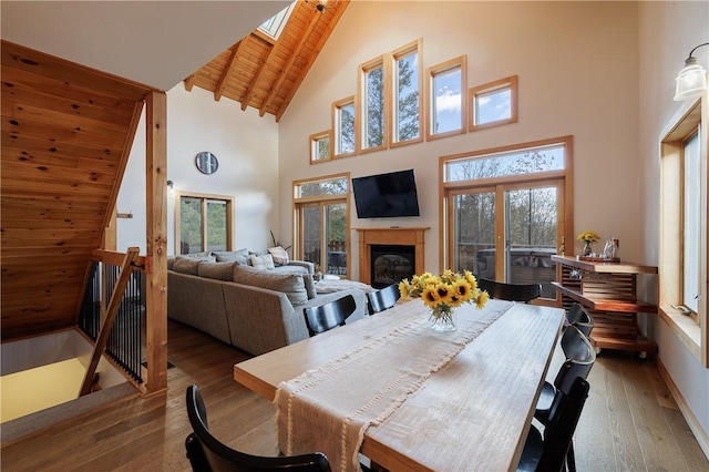 dining room featuring high vaulted ceiling, a skylight, wood ceiling, wood-type flooring, and a glass covered fireplace