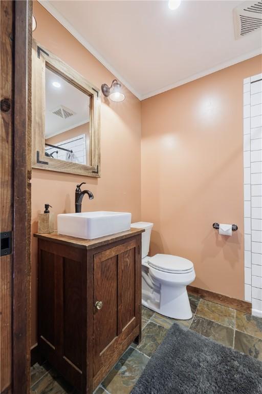 bathroom featuring visible vents, stone finish flooring, toilet, ornamental molding, and vanity