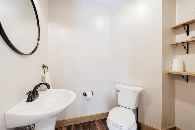 half bath featuring toilet, wood finished floors, baseboards, and a sink