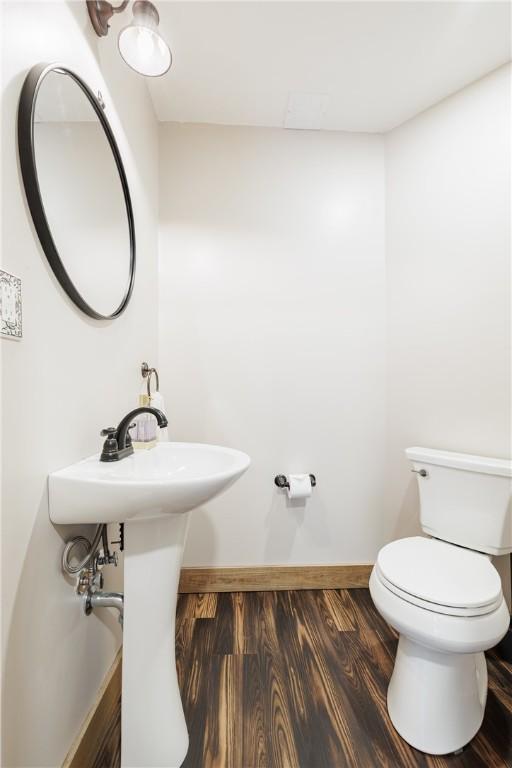 half bath with baseboards, toilet, and wood finished floors