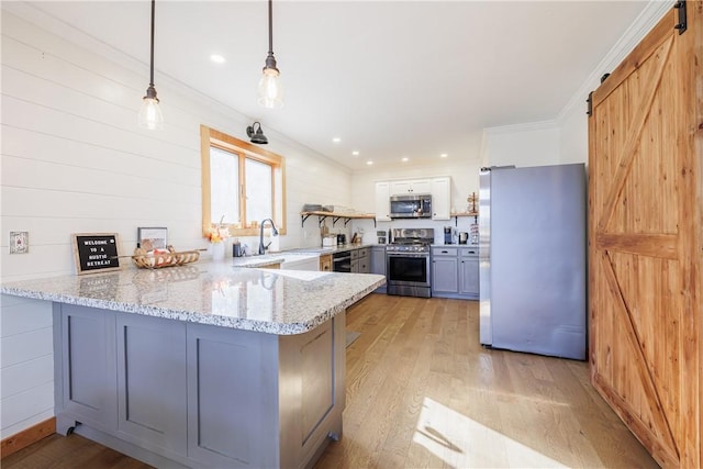 kitchen with light wood finished floors, a peninsula, a sink, appliances with stainless steel finishes, and a barn door