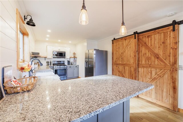 kitchen with a peninsula, ornamental molding, a sink, appliances with stainless steel finishes, and a barn door