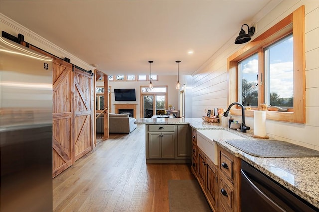 kitchen with light stone counters, light wood finished floors, a sink, stainless steel appliances, and a barn door