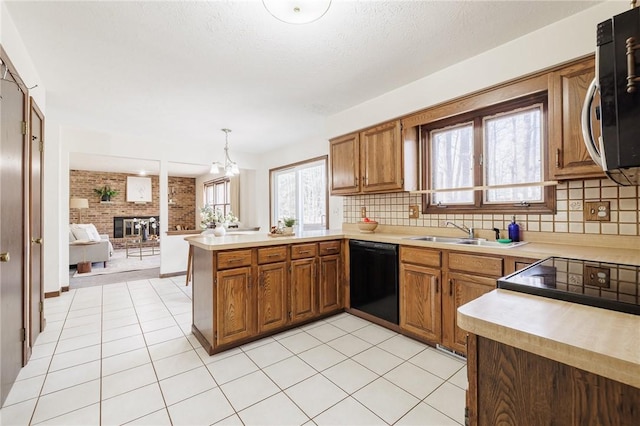 kitchen featuring stainless steel microwave, dishwasher, a peninsula, brown cabinetry, and a sink