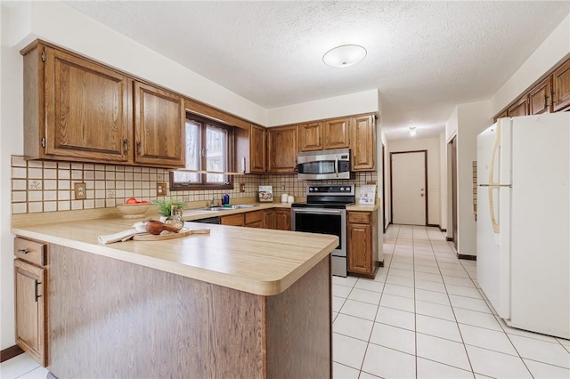 kitchen featuring a peninsula, light tile patterned flooring, decorative backsplash, light countertops, and appliances with stainless steel finishes