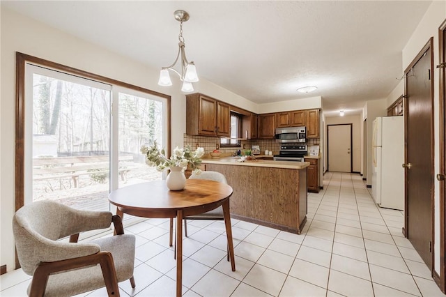 kitchen featuring decorative backsplash, brown cabinets, a peninsula, light tile patterned flooring, and stainless steel appliances