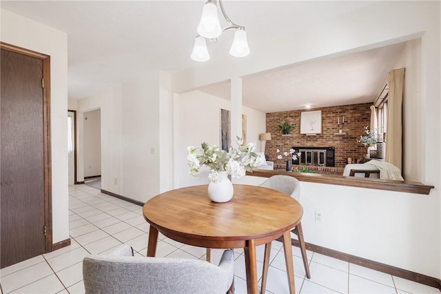 dining area featuring an inviting chandelier, a brick fireplace, light tile patterned floors, and baseboards