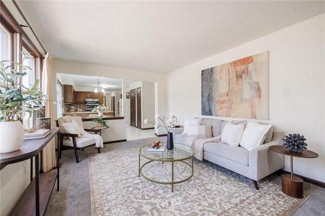 living room featuring baseboards, light carpet, and an inviting chandelier